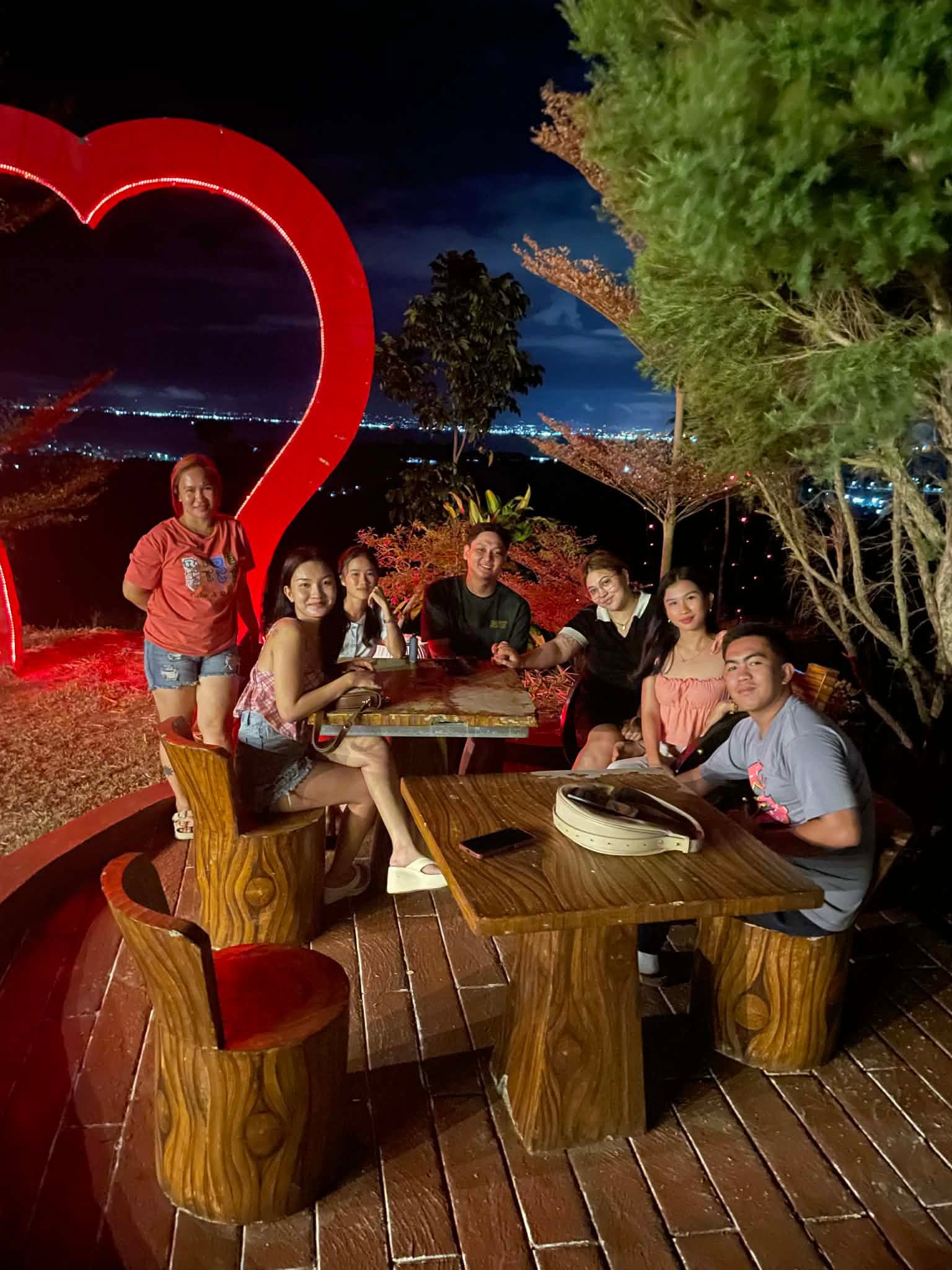 Evening gathering under the lit red heart arch with city lights below